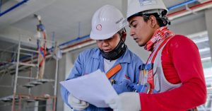 Two engineers in safety helmets reviewing construction plans at a worksite.